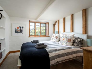 A bedroom with a double bed striped bedding and decorative pillows beside a window and wall art at Hope Cottage in Longborough