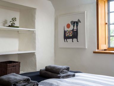 A bedroom with folded towels on a bed a wicker basket and a framed dog artwork on the wall at Hope Cottage in Longborough