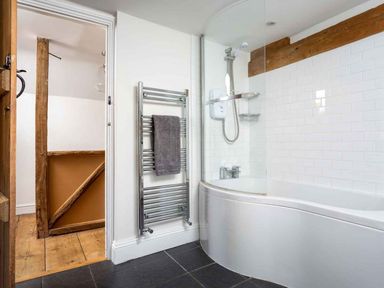A bathroom with a curved bathtub a shower an electric heated towel rail and wooden beams at Hope Cottage in Longborough
