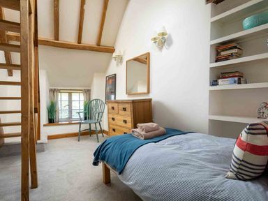 A bedroom with a single bed, wooden dresser, chair by a window, and a staircase at Hope Cottage in Longborough