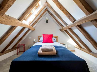 A single bed with folded towels on a blue blanket under a sloped ceiling with wooden beams at Hope Cottage in Longborough