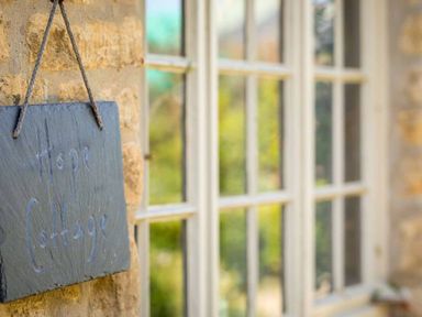 A sign reading Hope Cottage hanging on a stone wall next to a window at Hope Cottage in Longborough