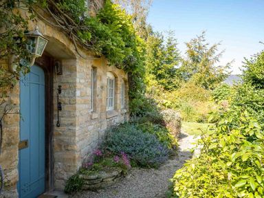 A stone cottage exterior with a blue door and surrounding garden at Hope Cottage in Longborough