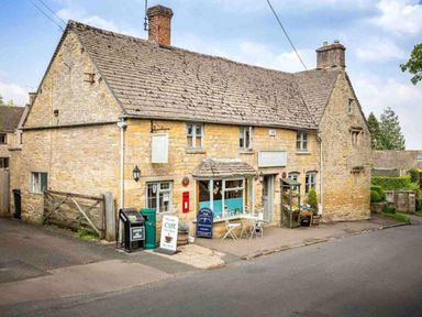 A stone building with a cafe sign tables and chairs outside by the roadside at Hope Cottage in Longborough