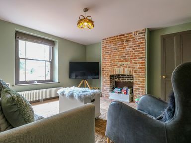 A living room with a brick fireplace a television on a stand and seating at Oak Cottage in Somerleyton