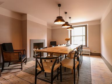 A dining room with a wooden table surrounded by chairs under three pendant lights at Oak Cottage in Somerleyton