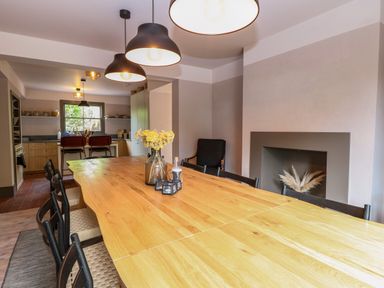 A dining area with a wooden table and black chairs a kitchen with bar stools and pendant lights at Oak Cottage in Somerleyton