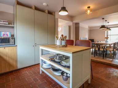 A kitchen with a wooden island holding kitchen utensils and bowls and a dining area with tables and chairs at Oak Cottage in Somerleyton