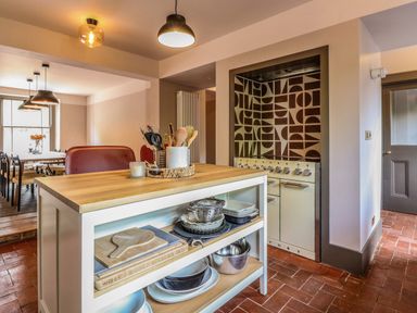 A kitchen with a wooden countertop island holding utensils and bowls next to a stove with a patterned backsplash at Oak Cottage in Somerleyton