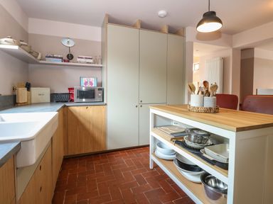 A kitchen with wooden cabinets a white sink a microwave on the counter and an island with utensils and bowls at Oak Cottage in Somerleyton