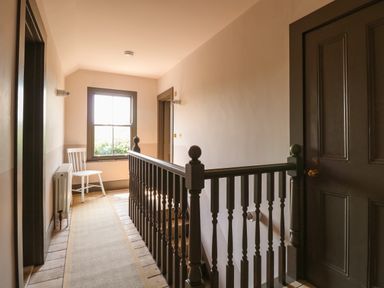 A hallway with a wooden railing a window and a white chair at Oak Cottage in Somerleyton