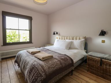 A bedroom with a bed folded towels on a blanket beside a window and wicker storage chests at Oak Cottage in Somerleyton