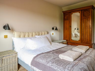 A bedroom with a bed with white pillows and blankets a wooden wardrobe with mirrored door and wicker baskets by the sides at Oak Cottage in Somerleyton