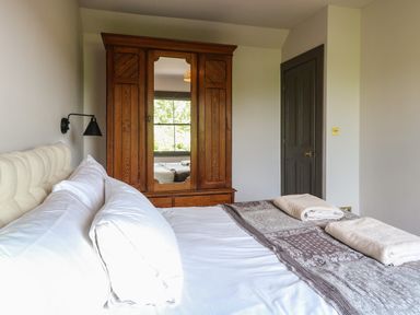 A bedroom with a bed white pillows a wooden wardrobe with a mirror and a closed door at Oak Cottage in Somerleyton