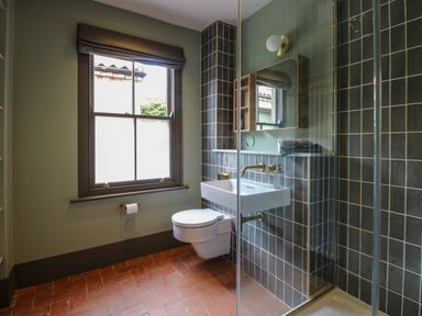 A bathroom with a wall-mounted toilet and sink a window with a blind and a shower enclosure with tiled walls at Oak Cottage in Somerleyton
