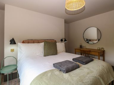 A bedroom with a bed with pillows and folded towels a green side table a wooden desk with a chair and a round mirror on the wall at Oak Cottage in Somerleyton