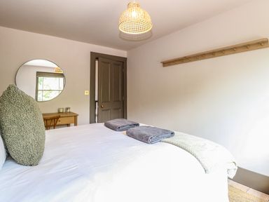 A bedroom with a bed two towels on it a round mirror above a wooden desk and a door at Oak Cottage Somerleyton