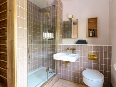 A bathroom with a tiled shower enclosure a wall-mounted sink a toilet and wooden shelves at Oak Cottage Somerleyton
