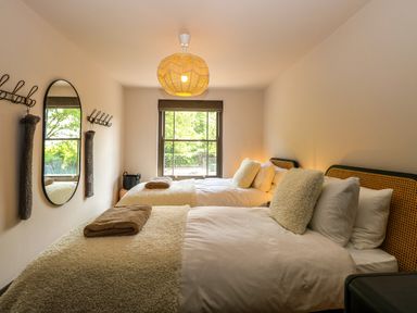 A bedroom with two single beds blankets and pillows near a window with a mirror on the wall at Oak Cottage in Somerleyton