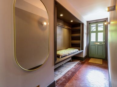 A hallway with a green door a built-in bench with cushion shelving and a wall mirror at Oak Cottage in Somerleyton