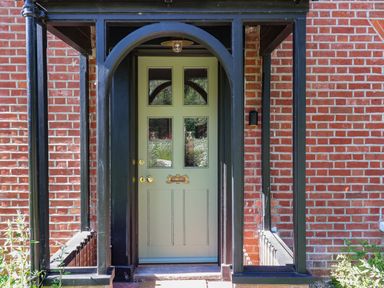 A green front door with four glass panels and a letterbox in a brick wall with black wooden frame