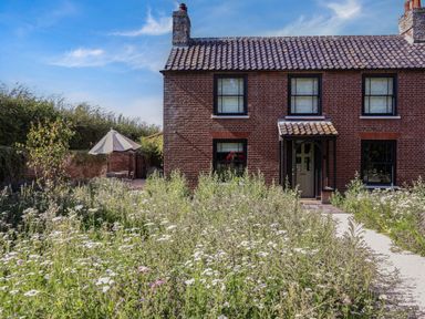 A brick house with tiled roof and four windows with a garden full of wildflowers and a patio umbrella at Oak Cottage in Somerleyton