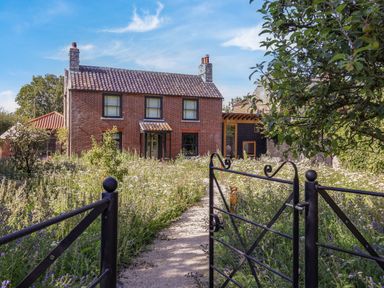 A red brick house with a tiled roof and a garden path leading through a black metal gate at Oak Cottage in Somerleyton
