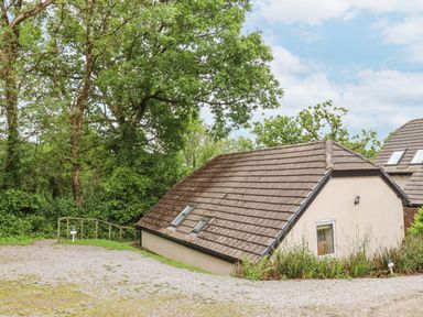 A sloped roof building surrounded by trees and gravel paths at Crystals in Hatherleigh