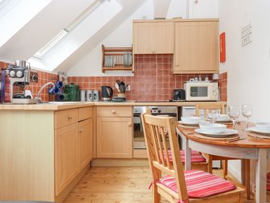 A kitchen with wooden cabinets and a dining table set with bowls and glasses at Crystals in Hatherleigh