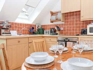 A kitchen with wooden cabinets, a dining table set with plates and glasses, a window above the sink and orange tiled backsplash at Crystals in Hatherleigh