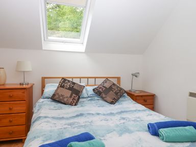 A bedroom with a bed between two wooden nightstands under a skylight window at Crystals in Hatherleigh
