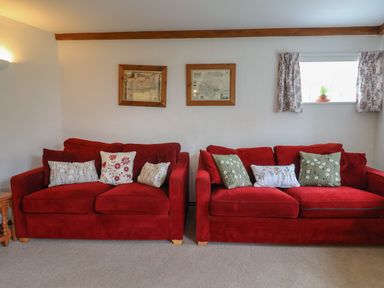 A living room with two red sofas and patterned cushions at Butterton Cottage Combe Raleigh near Honiton