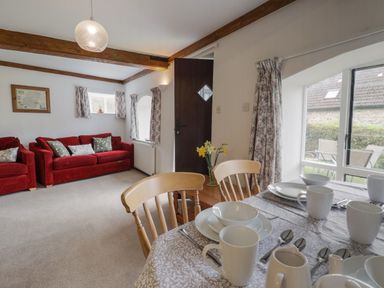 A living room with red sofas wooden dining chairs and a table set with white dishes at Butterton Cottage in Combe Raleigh near Honiton