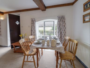A dining room with a wooden table set for four and wooden chairs near a window at Butterton Cottage in Combe Raleigh near Honiton