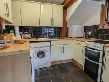 A kitchen with white cabinets, a washing machine, stove, microwave, wooden countertop and black tiled floor at Butterton Cottage in Combe Raleigh near Honiton