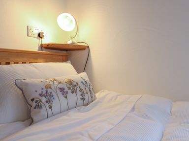 A bed with a floral embroidered pillow and a wall-mounted lamp at Butterton Cottage in Combe Raleigh near Honiton