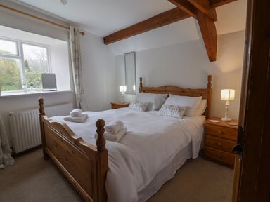 A bedroom with a wooden bed frame white bedding bedside tables with lamps and a window at Butterton Cottage Combe Raleigh near Honiton