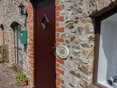 A stone cottage exterior with a wooden door a green mailbox and a plant pot at Butterton Cottage Combe Raleigh near Honiton