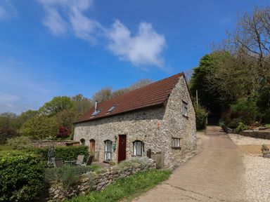 A stone cottage with a tiled roof and outdoor seating area near a paved driveway at Butterton Cottage Combe Raleigh near Honiton