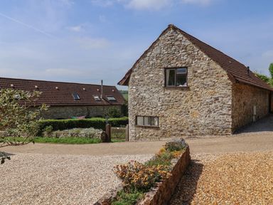 A gravel driveway leading to a stone house with a tiled roof and a garden gate at Butterton Cottage in Combe Raleigh near Honiton