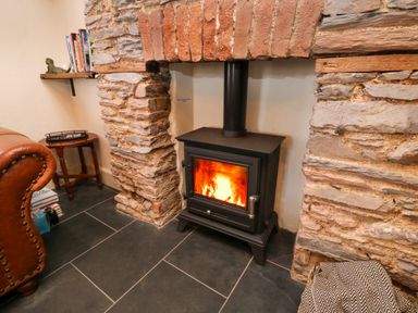 A wood burning stove inside a stone fireplace with a leather chair and a small table nearby at The Nook in Brixham