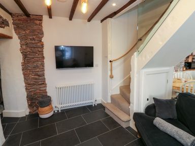 A room with a wall mounted TV radiator staircase and part of a sofa at The Nook in Brixham
