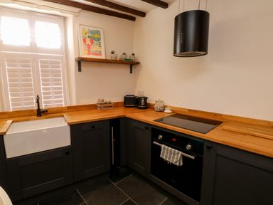 A kitchen with wooden countertops black cabinets a white sink a stove oven and a shelf with decorations at The Nook in Brixham