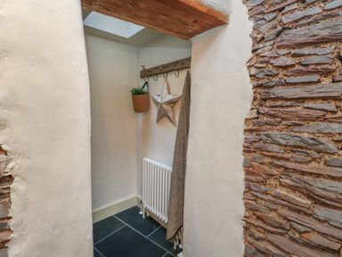 A hallway with a stone wall and hooks holding a plant pot a star decoration and a hanging cloth near a radiator at The Nook in Brixham