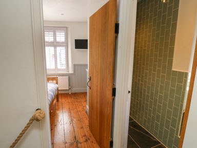 A bedroom with wooden floor and a bed visible through a door with a bathroom with green tiled walls next to it at The Nook in Brixham