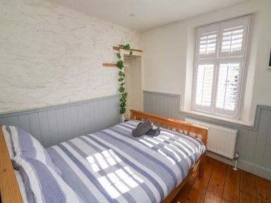 A bedroom with a wooden bed striped bedding a window with shutters and a plant hanging on the wall at The Nook in Brixham