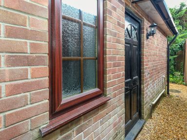 An outside view of a brick building with a wooden window and a black door with a wall light at Coldharbour Farm Bungalow Annexe in Coldharbour near Wareham