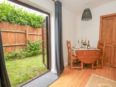 A dining area with a small wooden table set for two and chairs next to open glass doors leading to a garden at Coldharbour Farm Bungalow Annexe Coldharbour near Wareham
