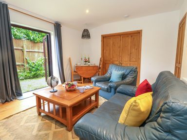 A living room with blue leather sofas a wooden coffee table and open doors to a garden at Coldharbour Farm Bungalow Annexe in Coldharbour near Wareham