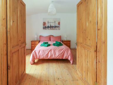 A bedroom with a double bed dressed in pink bedding and green towels on it two wooden nightstands with lamps and wooden doors at Coldharbour Farm Bungalow Annexe Coldharbour near Wareham